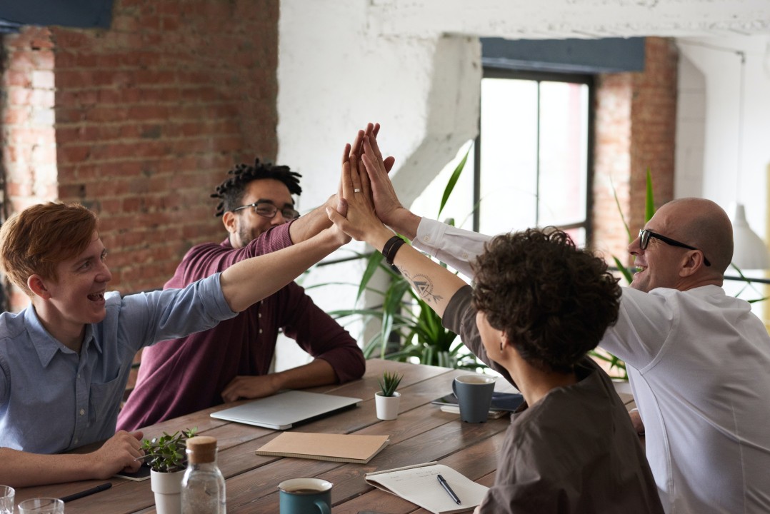 A group of business people hope and help each other by giving high fives in a meeting.